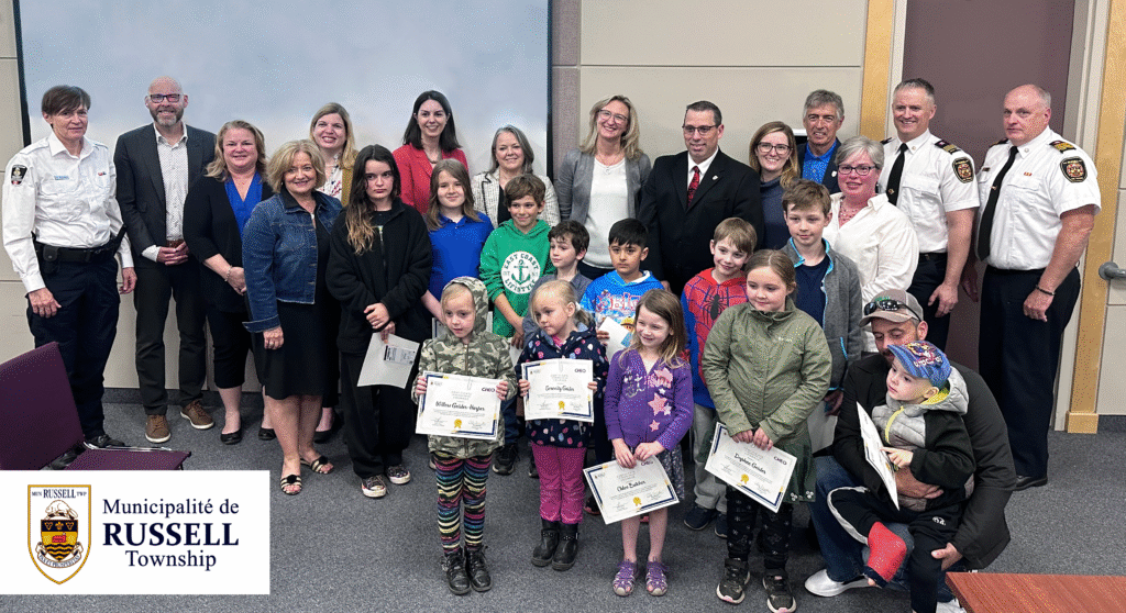 Shown in the photo in no particular order are Rory Renwick and the 11 children on the bus (Jake Vaughn, Nathan Vaughn, Levi Helmer, Amir Sakhizadeh, Chloe Butcher, Christopher Butcher, Nicholas Butcher, Daphne Geisler, Dylan Geisler, Serenity Geisler, and Willow Geisler-Harper), Tammy DeGiovanni (CHEO Senior VP, Clinical Services and Chief Nursing Executive), Jennifer Proulx (CHEO VP, Child Development and Community Services), Karen Macaulay (CHEO VP, Acute Care), Ron Ferguson (UCDSB Director), Susan Rutters (UCDSB Superintendent), Karina Parisien (UCDSP Trustee), Nichola Bond (Russell PS Principal), Erin O'Rourke (Russell PS Vice-Principal), Brian McBain and Ian Courville (Fire Chief & Deputy Fire Chief for Russell Township Fire Services), Millie Bourdeau (Director of Public Safety en Enforcement), Jamie Laurin (Interim Mayor), Lisa Deacon (Councillor), and Marc Lalonde (Councillor).