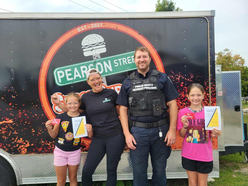 Saphyrëlle and Kaëlly Laroche proudly pose with Public Safety officer Jonathan Guidon after receiving a positive ticket for their civic-minded actions. The two young girls distinguished themselves by actively helping to keep Yahoo Park clean by picking up litter left behind, demonstrating their sense of responsibility and concern for the environment. To recognize their actions, they each received a Tim Hortons gift card, a small token of encouragement that reflects the importance of positive community initiatives.