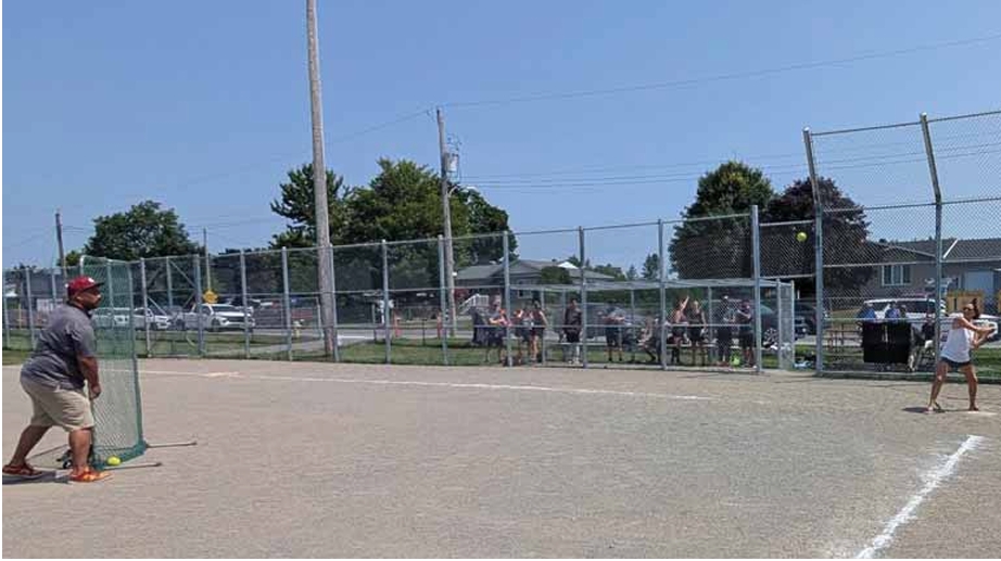 Le conseiller Simon-Olivier Péladeau-Houle effectue le premier lancer cérémonial tandis que Julie Henrie, présidente du Club Optimiste St-Pascal Baylon 2025-2026 et présidente de la Ligue mixte de baseball St-Pascal, se tient au marbre dans le but de frapper la balle pour commémorer officiellement la rénovation du terrain de baseball du parc St-Pascal, le 28 juillet.