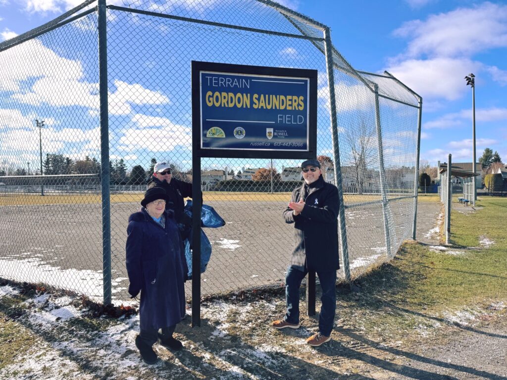 Councilor Jamie Laurin (top left) and Mike Tarnowski (right) help uncover the new Gordon Saunders sign with the help of the family’s representative.