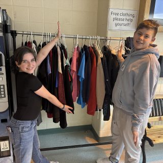 Russell High School Grade 8 students and Thrifty T’s group members Zoe Coutlee and Jacob Lopes show off a rack of free upcycled clothing located near the front entrance of the school.