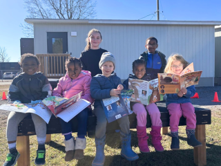 Les élèves de l’ÉÉC Sainte-Trinité écoutent attentivement les histoires de Robert Munsch, lues par les élèves de 6ᵉ année dans la cour d’école.